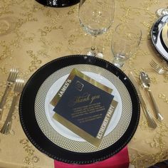 a black and gold table setting with place cards, silverware, and wine glasses