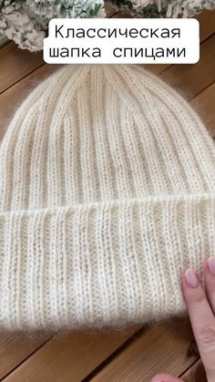 someone is holding their hand near a white knitted beanie