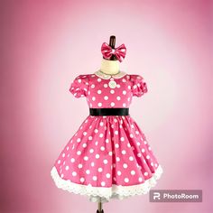 a pink dress with white polka dots and a black bow on the front, sitting on a mannequin