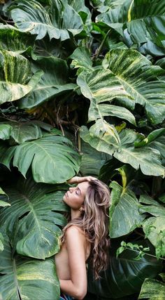 a woman standing in front of large green leaves with her head resting on her hands