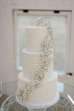 a three tiered white cake with flowers on the top and bottom is sitting on a glass table