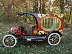 an old fashioned car is parked on the grass in front of some trees and leaves