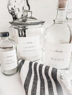 three bottles with labels on them sitting next to a towel and a glass jar filled with liquid