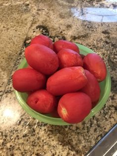 a green bowl filled with red fruit on top of a counter