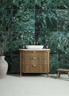 a bathroom with green marble walls and flooring next to a white sink on top of a wooden cabinet