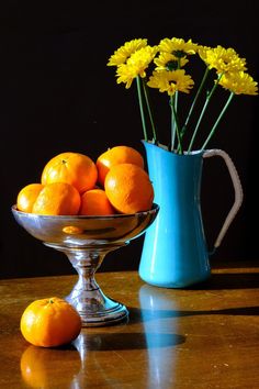 oranges and daisies in a blue vase on a wooden table with a black background