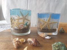 two glass candles with starfish on them sitting on a table next to seashells