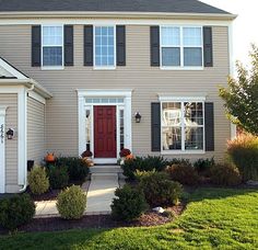 a large house with two red doors and black shutters on the front, surrounded by green grass