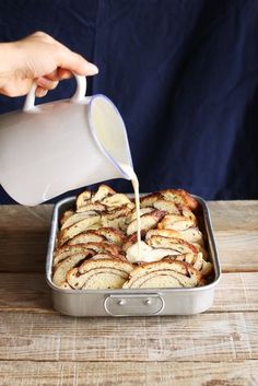 a person pouring milk over some food in a pan on top of a wooden table