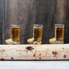 three shot glasses filled with beer sitting on top of a piece of wood