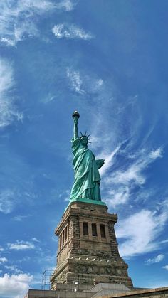 the statue of liberty stands tall in front of a blue sky with wispy clouds