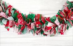 a red and green christmas wreath on a white wooden background with snowflakes hanging from it's sides