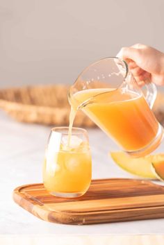 someone pouring orange juice into a glass on top of a wooden tray with slices of melon