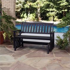 a wooden bench sitting next to a pool surrounded by trees and plants on a patio