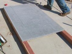 a man standing next to a large piece of wood on top of a cement floor