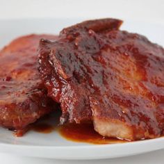 two pieces of meat sitting on top of a white plate covered in bbq sauce