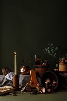 a table topped with lots of different types of items next to a candle and potted plant