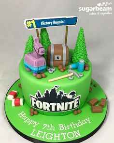 a green birthday cake with fortnite decorations on top and a sign that says fortnite happy 7th birthday leighton