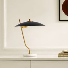 a table lamp sitting on top of a white dresser next to a painting and books