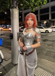 a woman dressed in silver is standing on the street with a cane and wearing a costume