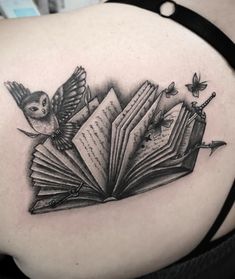 an open book tattoo on the back of a woman's shoulder with birds flying around it