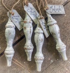 four white painted wooden handles with tags attached to them on a wood surface, some are hanging from twine strings