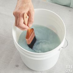 a person with a brush in a bucket filled with blue water and foamy liquid