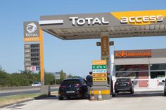 several cars are parked in front of a total access gas station on the side of the road