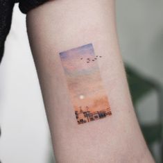 a small watercolor tattoo on the arm of a woman's left arm, with an image of a lighthouse and birds flying in the sky