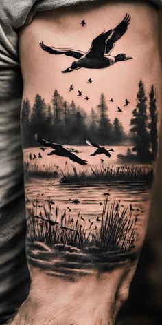 a man's arm with some birds flying over the water and trees on it