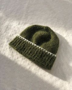 a green knitted beanie laying on top of a white sheet with holes in it