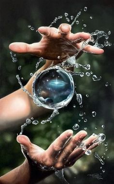 two hands are holding an object in the air with water splashing on it and trees behind them