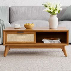 a coffee table with a bowl of flowers on it next to a couch and pillows