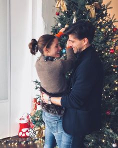 a man and woman standing in front of a christmas tree