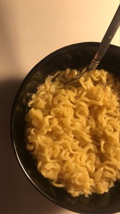 a black bowl filled with noodles on top of a white counter next to a spoon