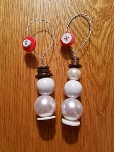 two white and red beads are attached to earwires on a wooden surface,