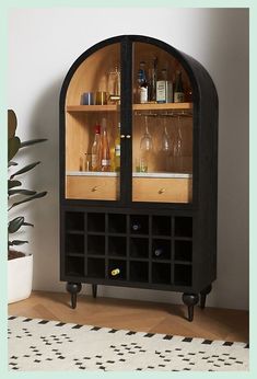 a black cabinet with wine glasses and bottles on the top shelf in front of a potted plant