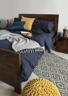 a bed with blue sheets and yellow pillows on it, next to a gray rug