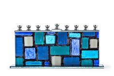 PRICES MAY VARY. HANDCRAFTED GLASS WALL: Silver candle holders stand atop a wall of glass with aqua, turquoise, cerulean blue, navy & white “stones” resembling the Kotel to make this glass menorah an artwork. A TIMELESS TRADITION: The contemporary menorah features a wall design with a twist of color. It meets all halachic requirements. Celebrate the holiday and light up the night! QUALITY CRAFTED: Made with premium grade materials, and high quality construction, our menorahs for chanukah stand s Glass Menorah, Chanukah Menorah, Silver Candle Holders, Hanukkah Candles, Standing Candle Holders, Silver Candle, Western Wall, Hanukkah Menorah, Selling Candles