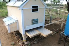 a small white chicken house sitting on top of a pile of dirt next to a blue barrel