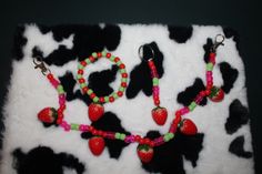 two necklaces with strawberries and green beads are on a cow print background,