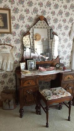 an old fashioned dressing table and stool in a room with floral wall paper on the walls