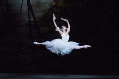 a ballerina in the air with her arms outstretched and legs spread out, while she is wearing a white tutu