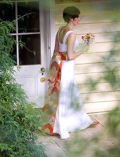 a woman in a white dress is holding a bouquet and walking out the door to her house