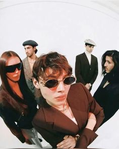 a group of people standing next to each other in front of a white wall with sunglasses on