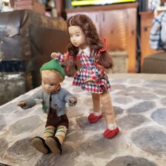 two dolls sitting on top of a table next to each other