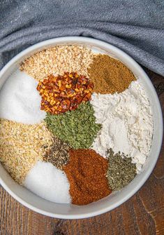 a white bowl filled with different types of spices and seasoning on top of a wooden table