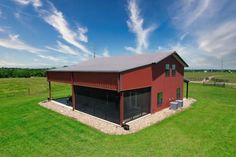 an aerial view of a red barn in the middle of a green field with blue skies