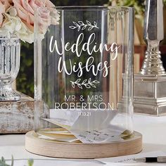 a clear glass vase filled with flowers next to a couple's wedding wishes sign