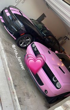 two pink sports cars parked next to each other in front of a garage with a heart on the hood